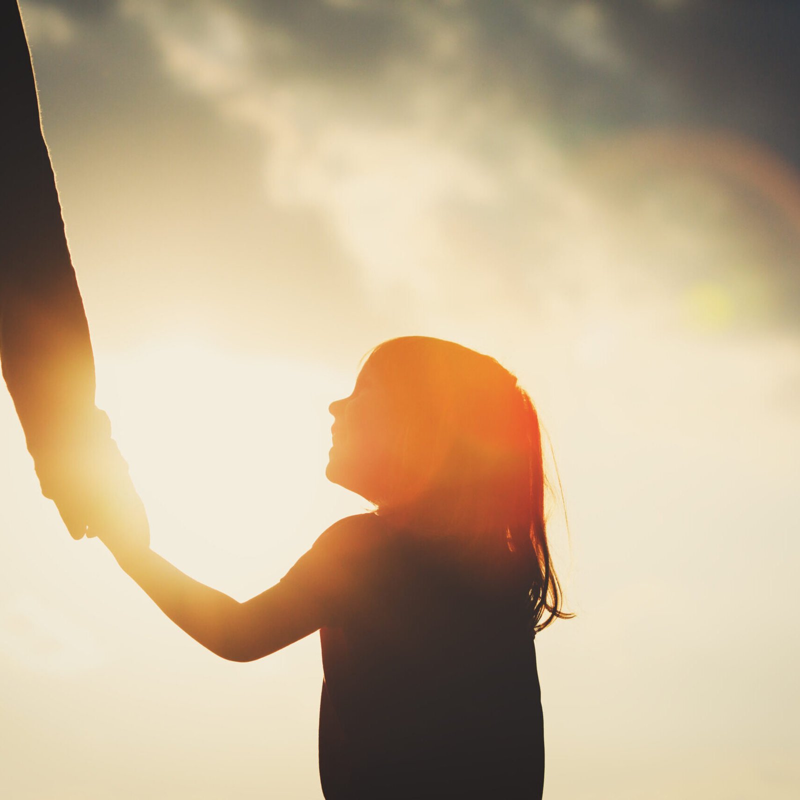 silhouette of little girl holding parent hand at sunset sky